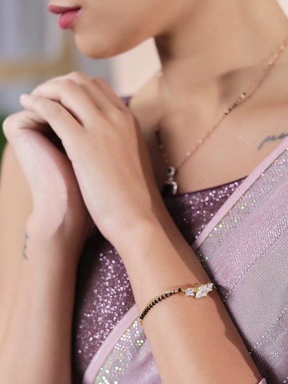 Closeup of a woman wearing a small mangalsutra design bracelet with black beads and sparkling stones, paired with a pastel saree.