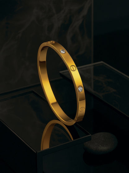 A stylish gold bracelet design for women featuring embedded crystals, displayed on a reflective black pedestal.