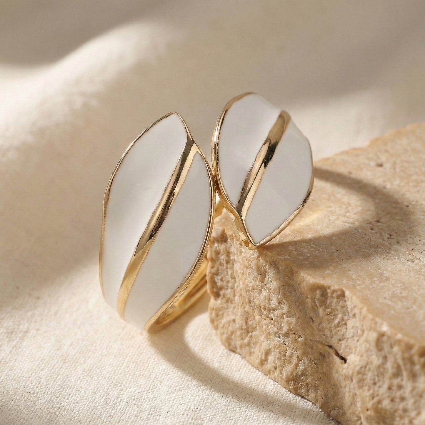 stylish gold bracelet design for women featuring white enamel leaf patterns on a stone display.