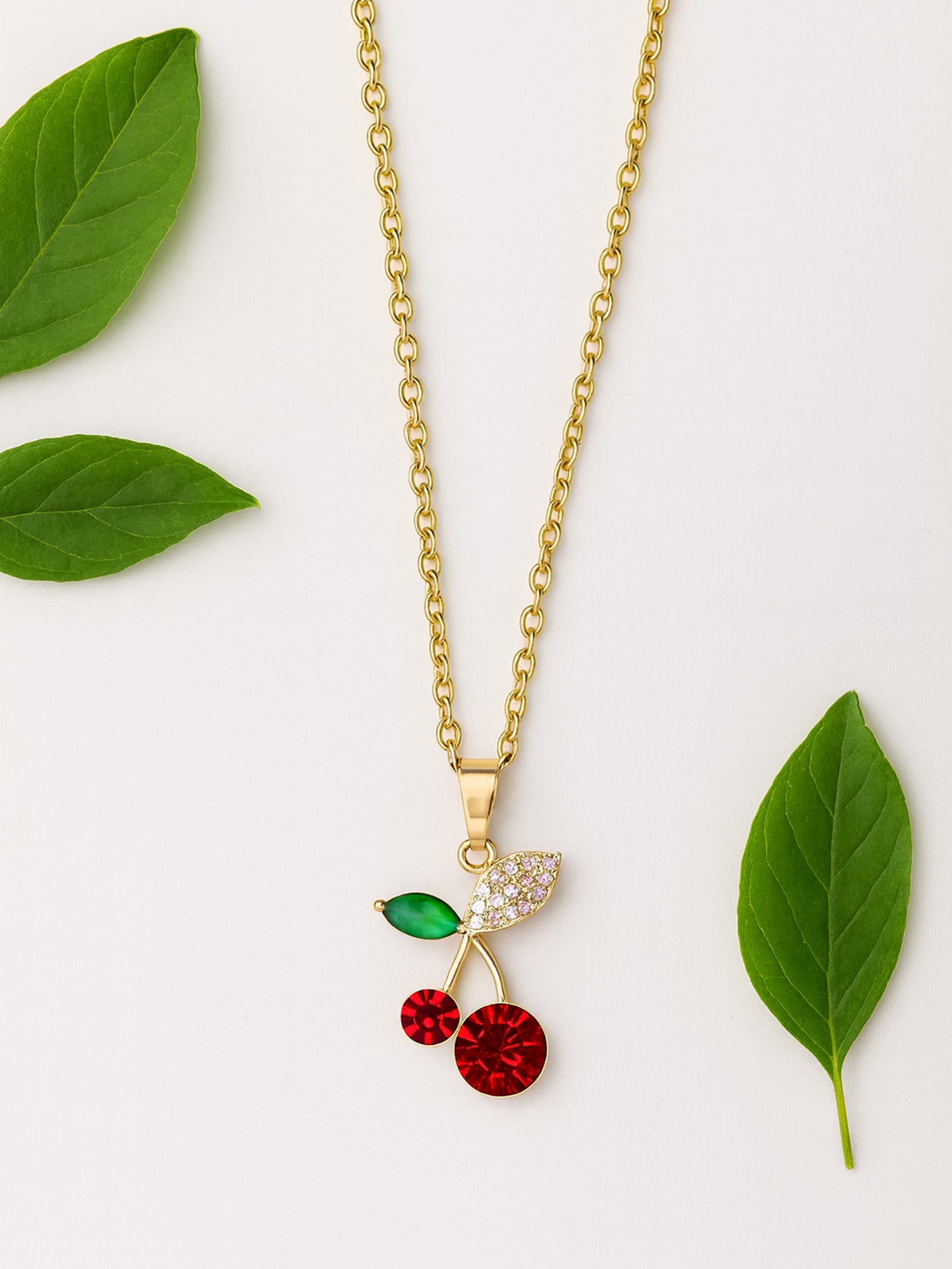 Close-up of a high-quality gold chain with pendant showcasing a cherry-shaped charm with shimmering red faceted gemstones and a detailed pavé leaf.