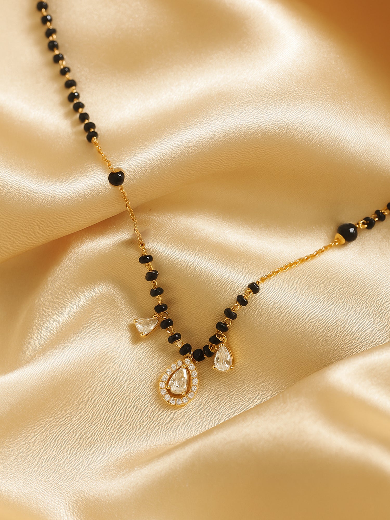 Minimal gold mangalsutra with black beads, fine gold chain and teardrop crystal pendant on satin fabric