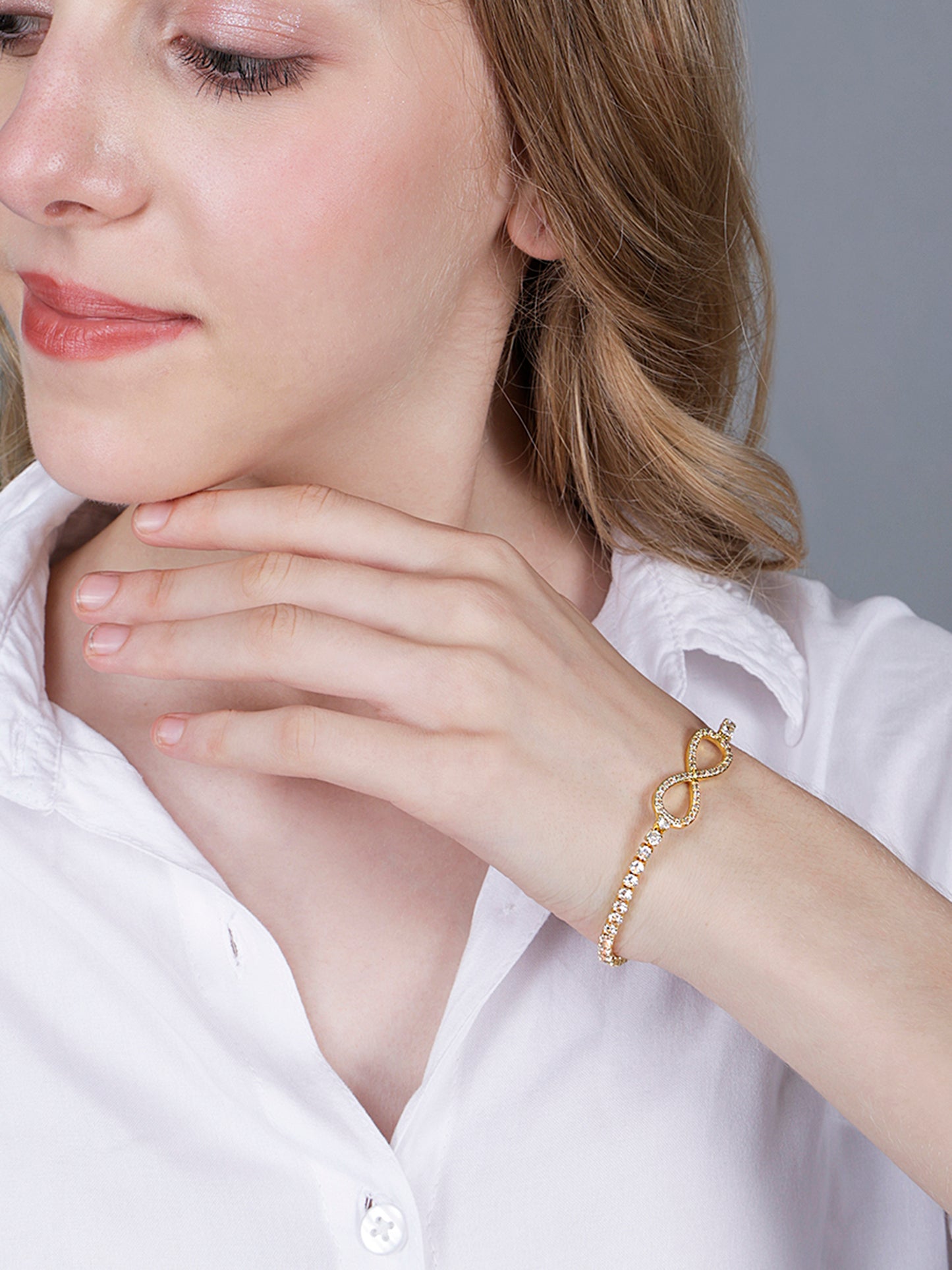 Gold bracelet design featuring a crystal-studded infinity symbol on a champagne silk background.