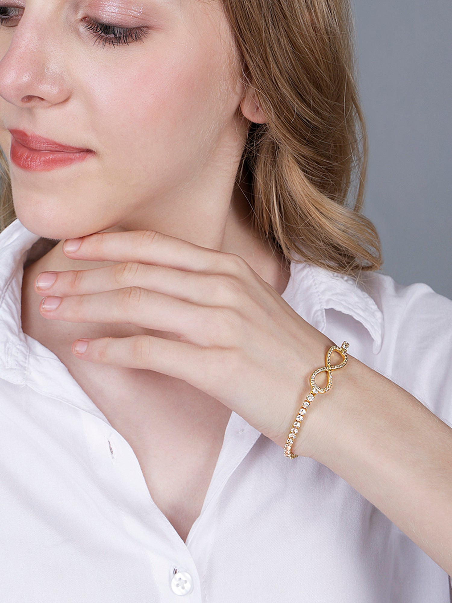 Gold bracelet design featuring a crystal-studded infinity symbol on a champagne silk background.