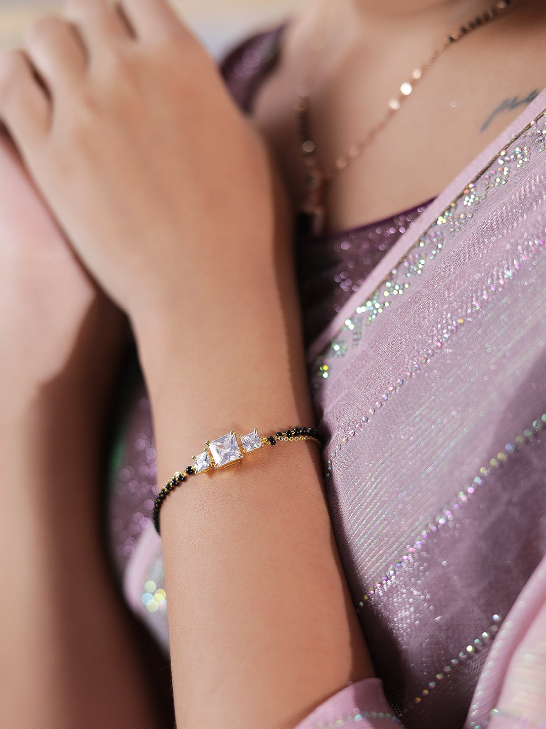 Women’s mangalsutra design bracelet with gold chains, black beads, and a three-stone centerpiece on the wrist