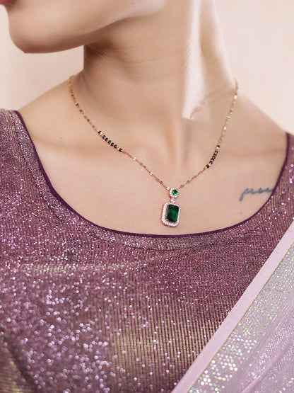 Traditional mangalsutra design with a gold chain and emerald pendant, shown close-up on a model wearing a shimmer saree