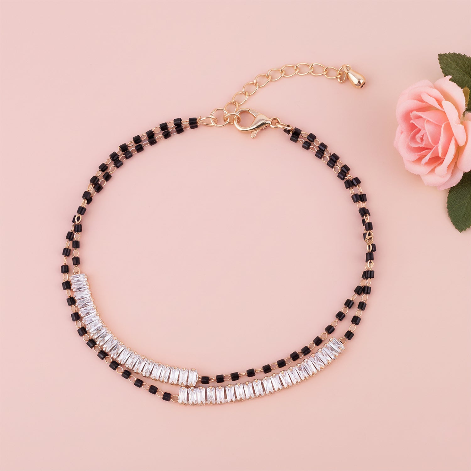 Traditional mangalsutra design bracelet with dual black beads and sparkling stone accents on a soft pink background.