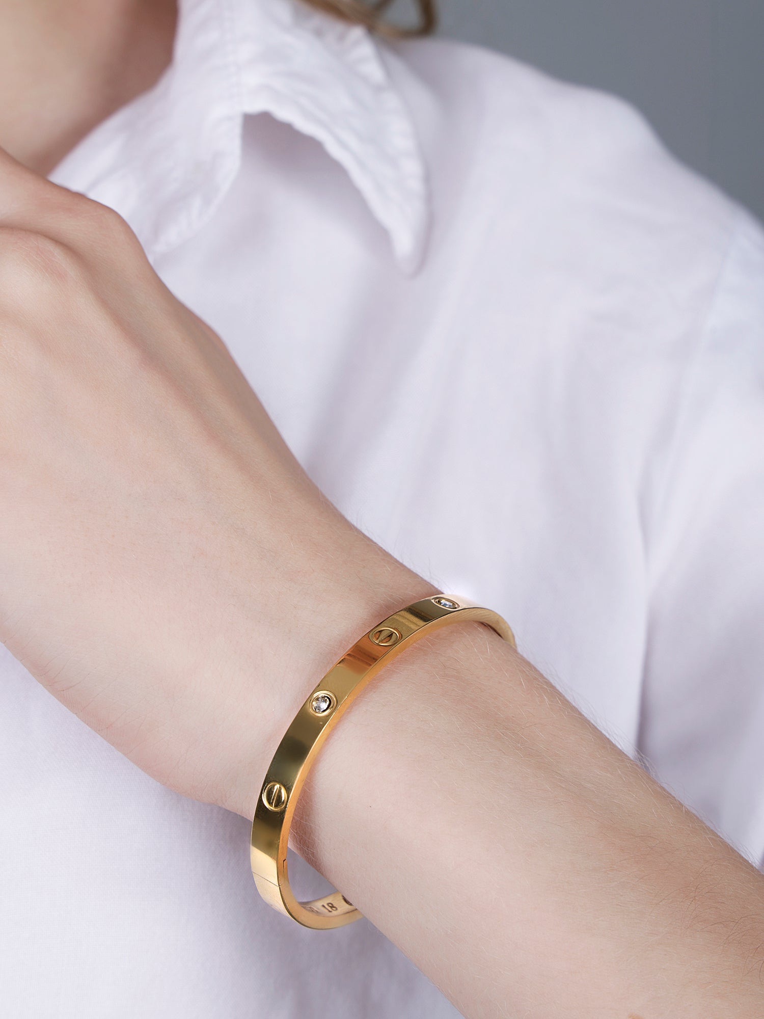 Close-up shot of a high-shine gold bracelet for women worn on a wrist with a white button-down shirt.