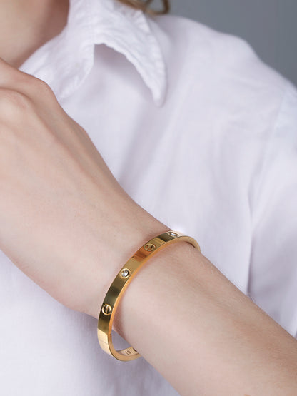 Close-up shot of a high-shine gold bracelet for women worn on a wrist with a white button-down shirt.
