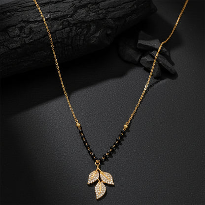 Gold plated mangalsutra design with black beads and a crystal leaf pendant on a dark textured background