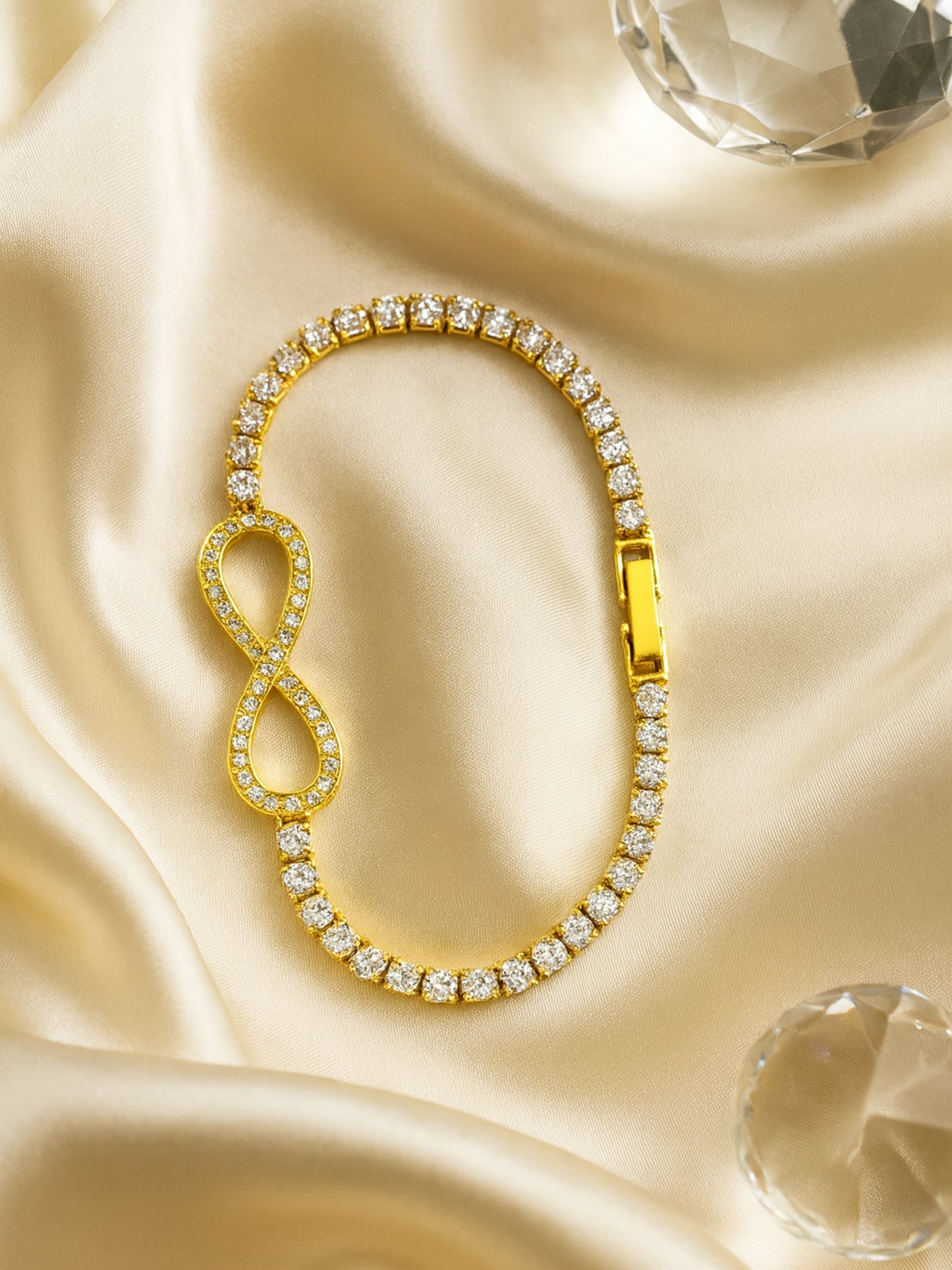 Latest bracelet design with a gold-toned infinity motif and round-cut crystals on a dark earthy background.