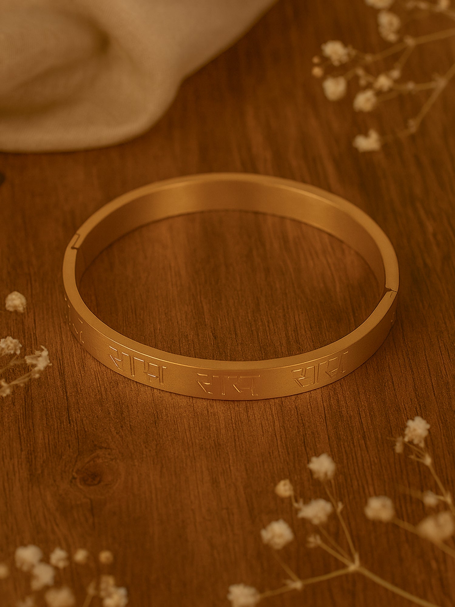 A simple bracelet for women with a sleek gold band and Devanagari script engraving on a wooden surface.
