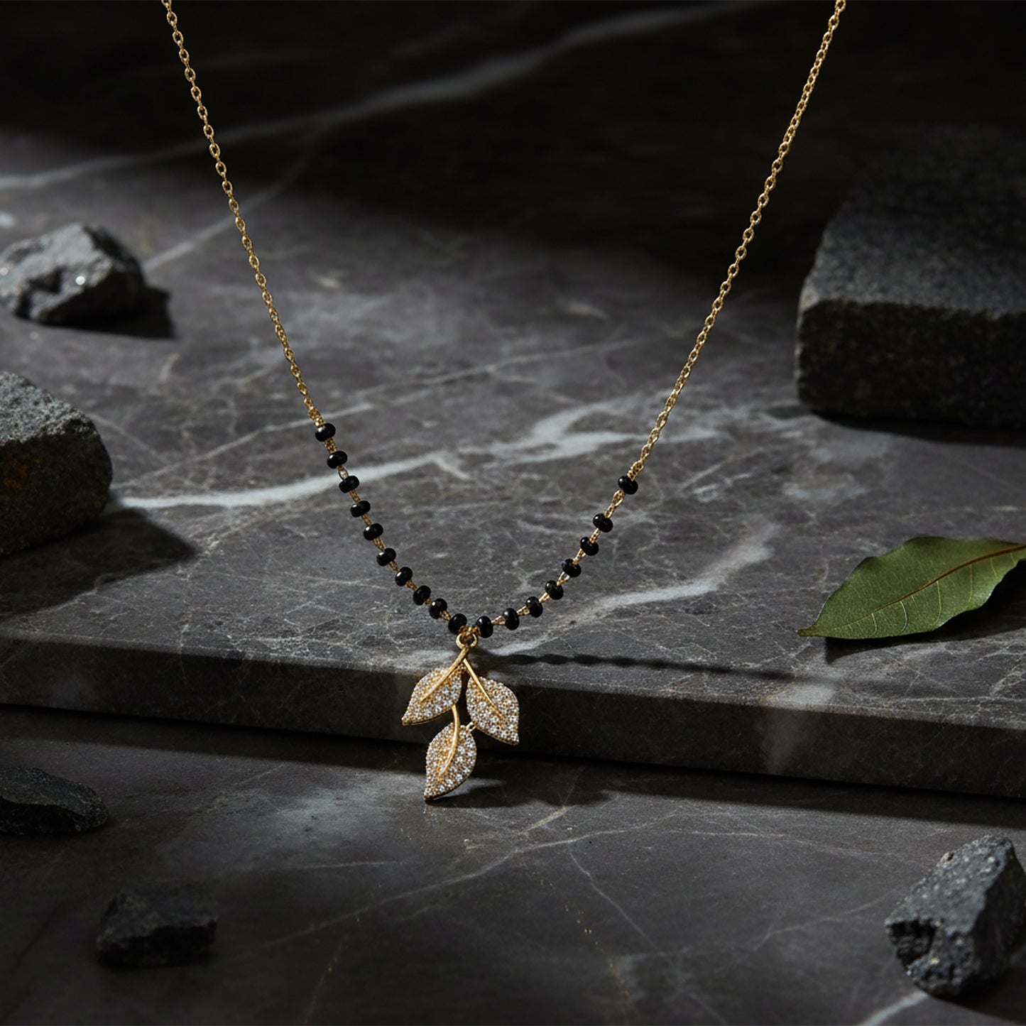 Small mangalsutra design in gold with black beads and leaf pendant displayed on a marble surface