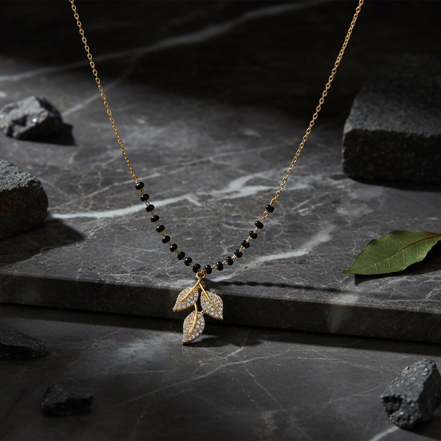 Small mangalsutra design in gold with black beads and leaf pendant displayed on a marble surface