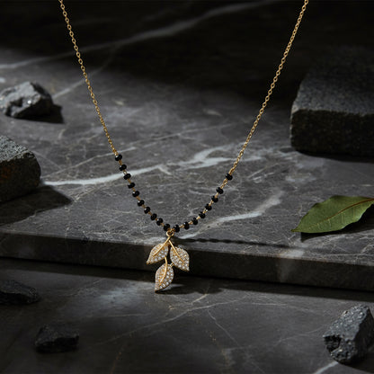 Small mangalsutra design in gold with black beads and leaf pendant displayed on a marble surface