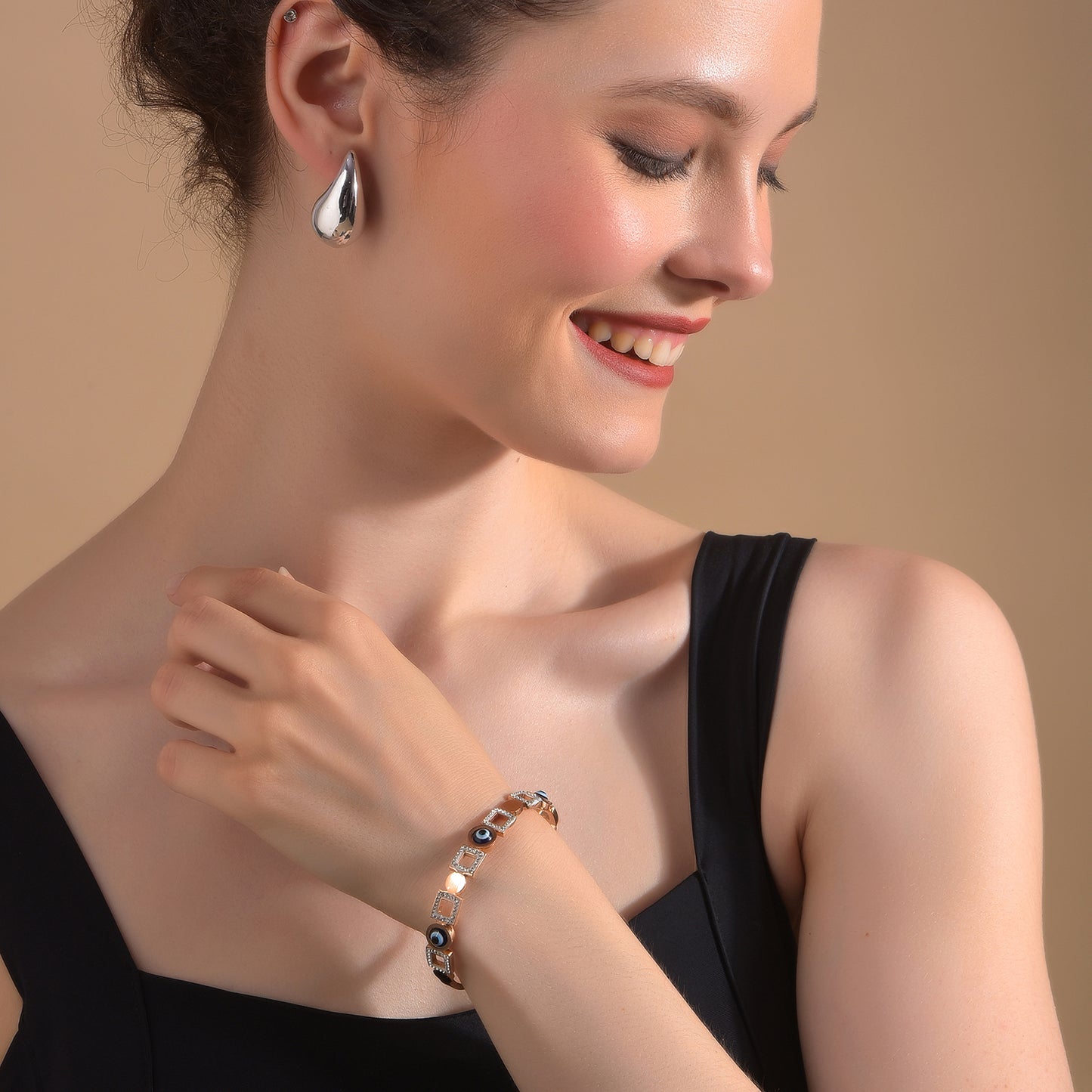 A stylish gold bracelet design for women worn with an elegant black dress and silver earrings.