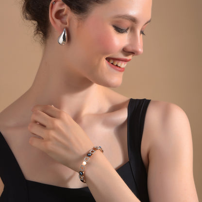 A stylish gold bracelet design for women worn with an elegant black dress and silver earrings.